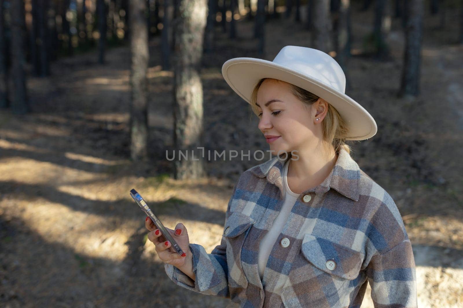 Autumn portrait of a smiling woman holding a phone against the background of the forest Happy girl using a mobile phone alone in the forest in nature in autumn. Copy space by malyshph