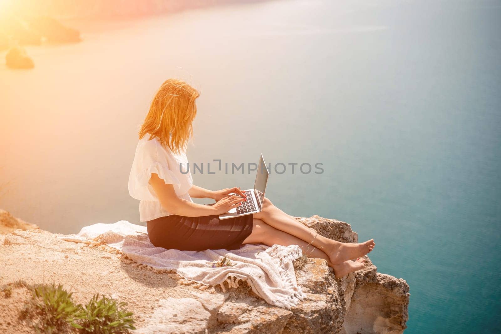 Freelance woman working on a laptop by the sea, typing away on the keyboard while enjoying the beautiful view, highlighting the idea of remote work. by Matiunina