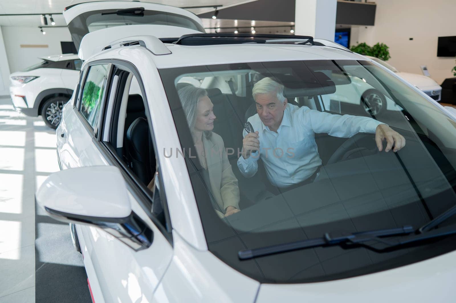 Mature Caucasian couple sitting in a new car and rejoicing at the purchase. View through the windshield