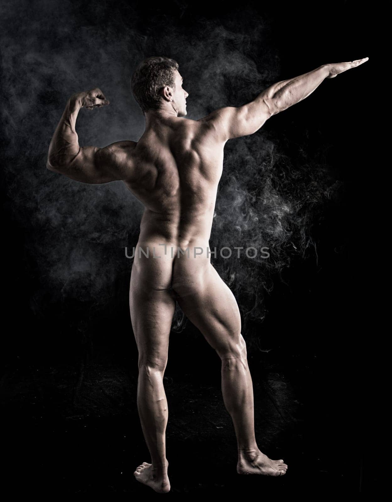 Full Body Shot of Fit Naked Bodybuilder Man Striking a Pose Facing Back, on Dark Background.