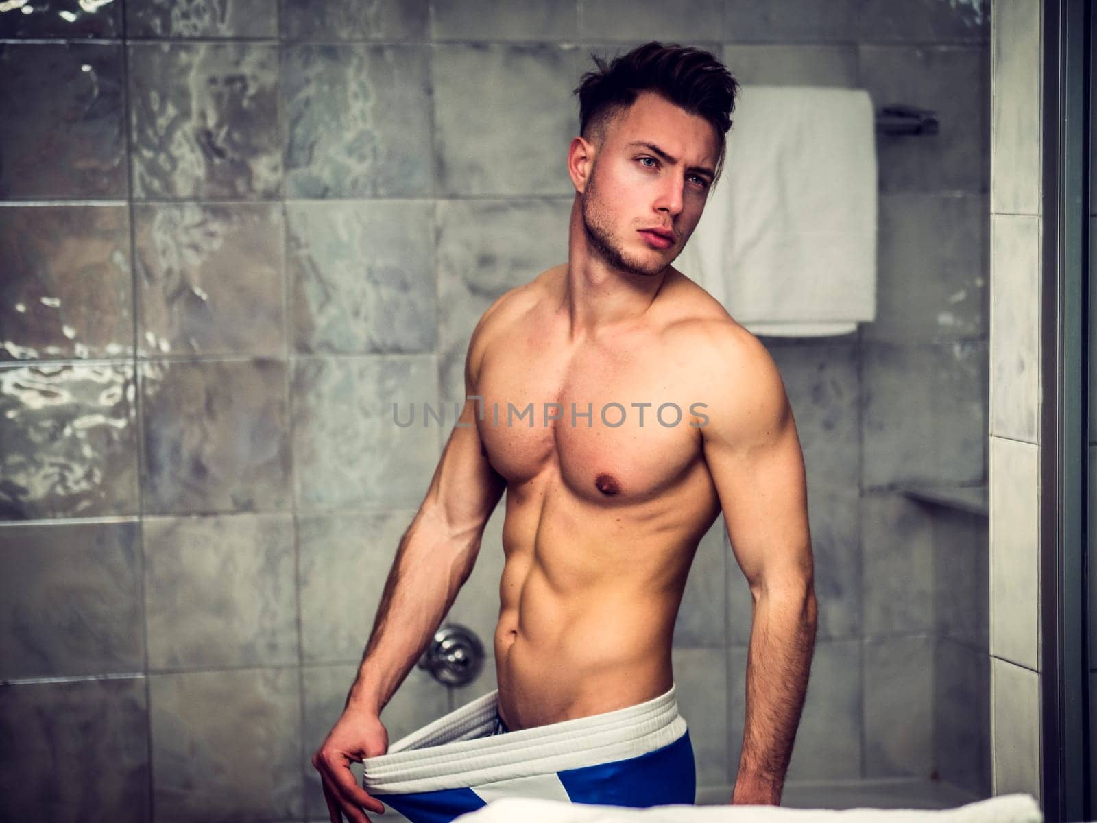 A shirtless man standing in front of a shower