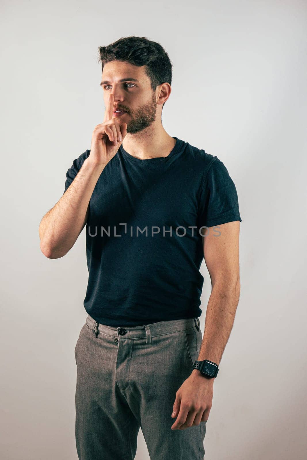 Hush. Young handsome man silencing you, saying shut up, in studio shot. Young man doing hush sign with finger over his mouth, looking at camera, silencing