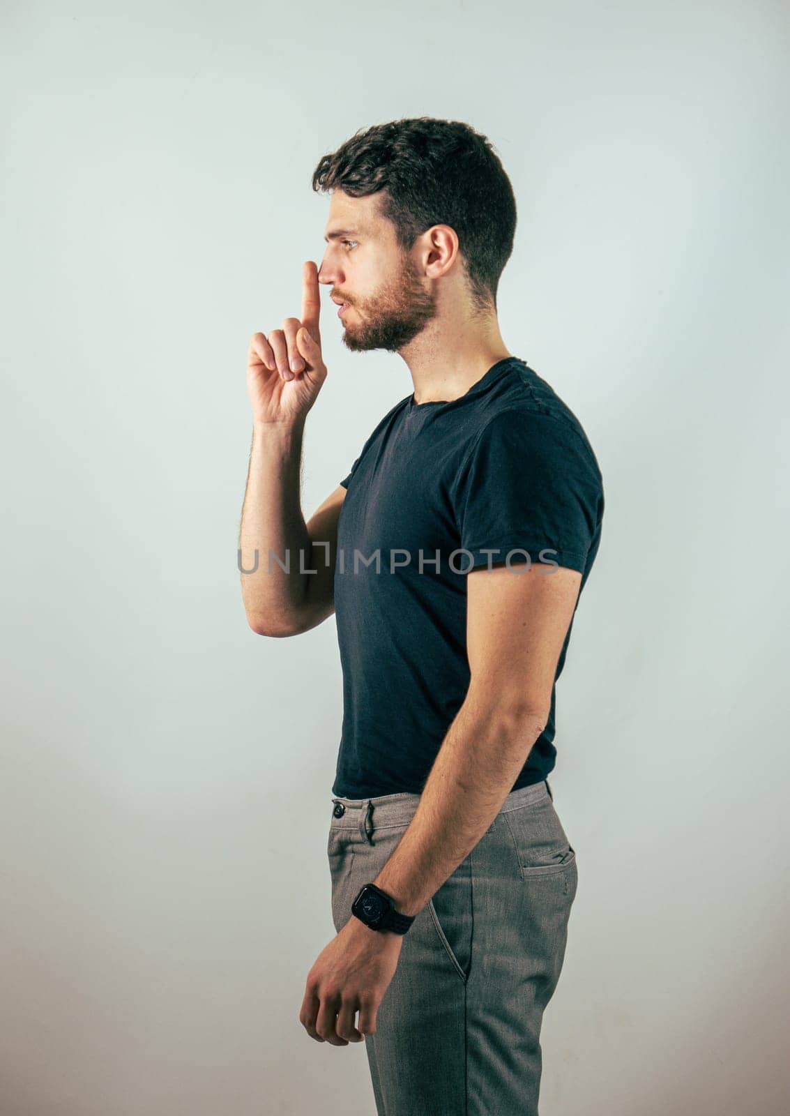 Hush. Young handsome man silencing you, saying shut up, in studio shot. Young man doing hush sign with finger over his mouth, looking at camera, silencing