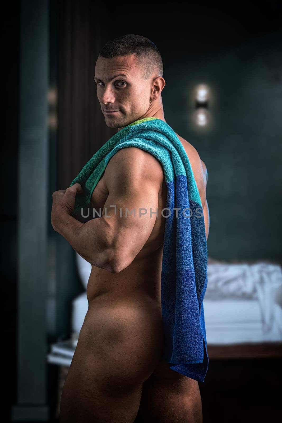 Completely naked handsome muscular man looking at camera in bedroom after shower