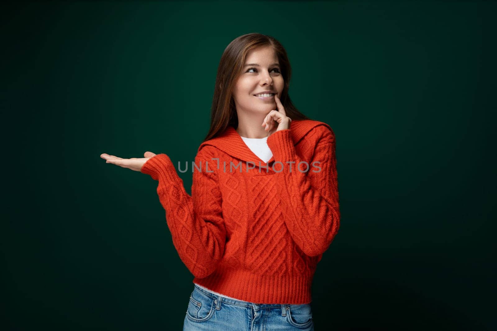 Dreamy 30 year old woman with brown hair in a red sweater on a green dark background.