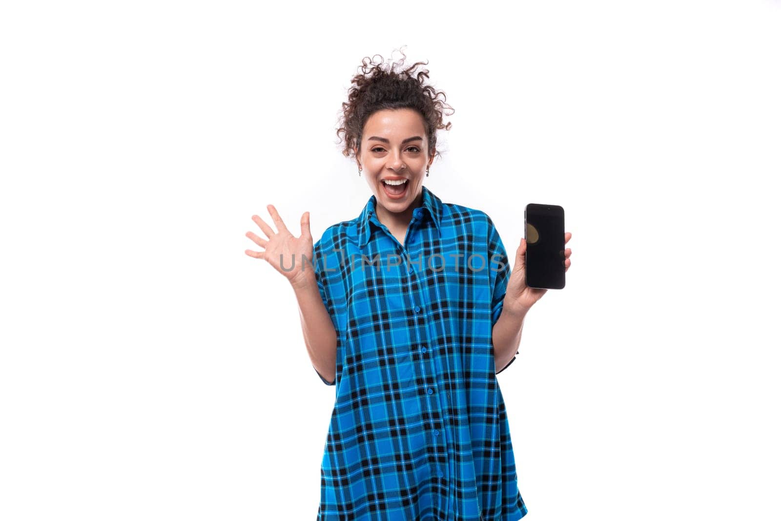 young cute curly brunette woman in blue plaid shirt showing phone screen.