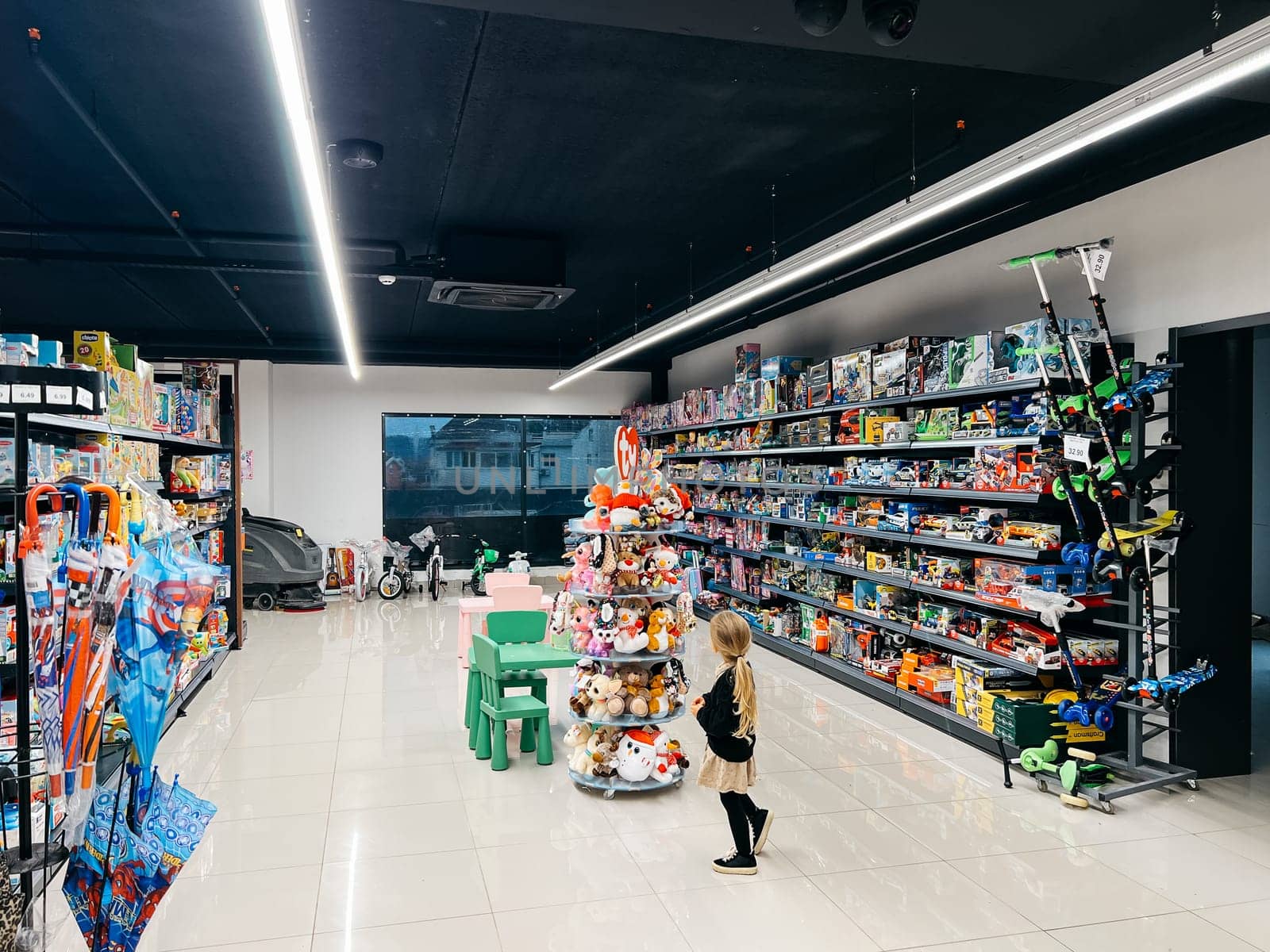 Little girl stands near a toy rack in a supermarket. Back view. High quality photo