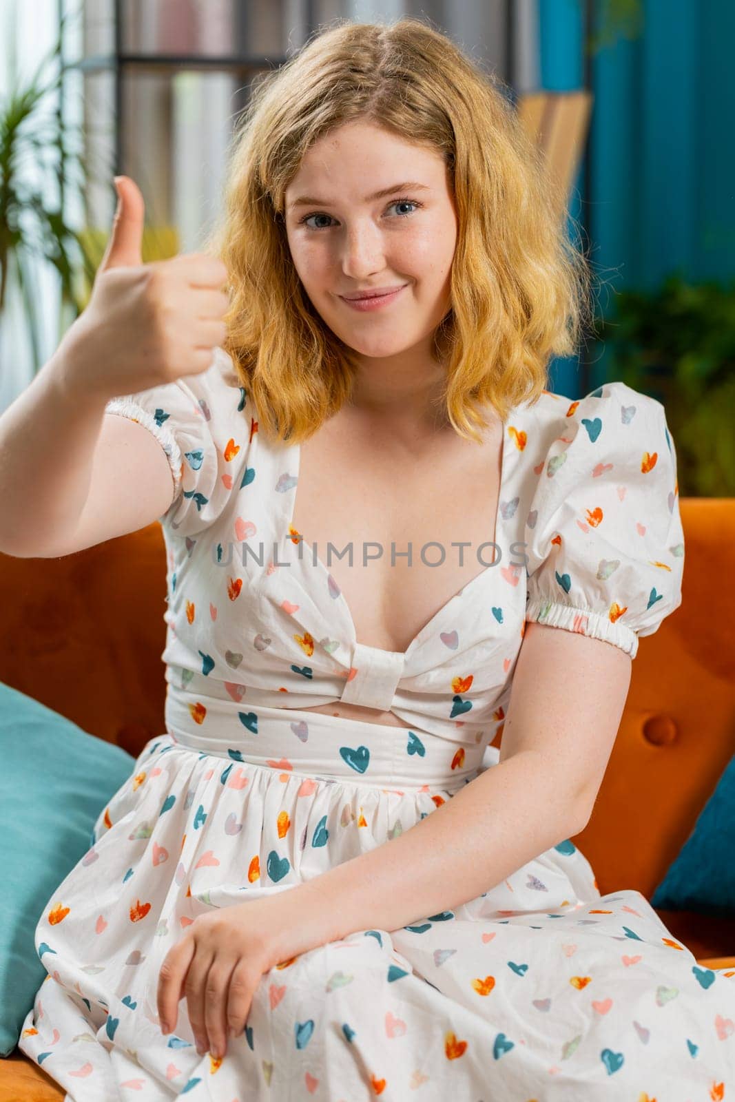 Like. Happy excited redhead woman looking approvingly at camera showing thumbs up, like sign positive something, good great news, positive feedback. Young girl sitting on couch at home room. Vertical