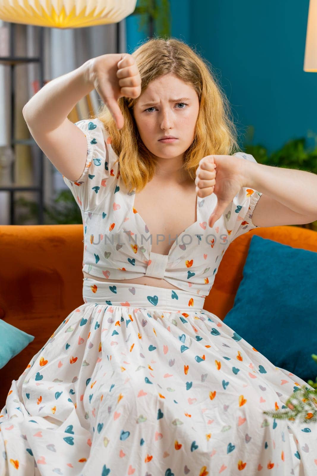Upset young woman showing thumbs down, dislike bad work, disapproval, dissatisfied feedback at home by efuror