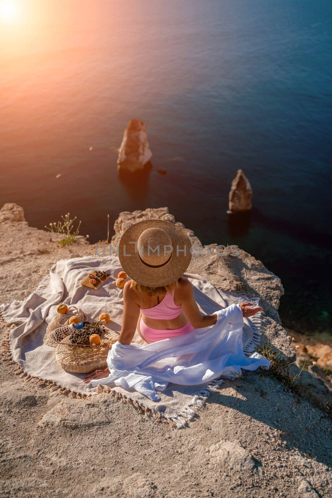 woman sea trevel. photo of a beautiful woman with long blond hair in a pink shirt and denim shorts and a hat having a picnic on a hill overlooking the sea.