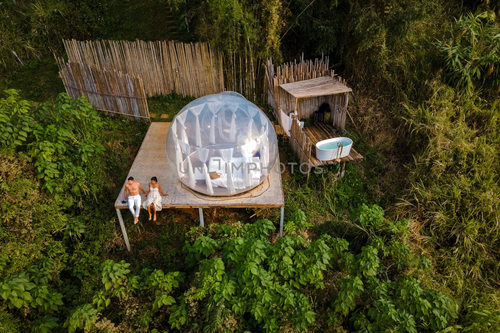 couple man and women in a bubble tent with an outdoor bathroom with bath in the jungle rainforest by fokkebok