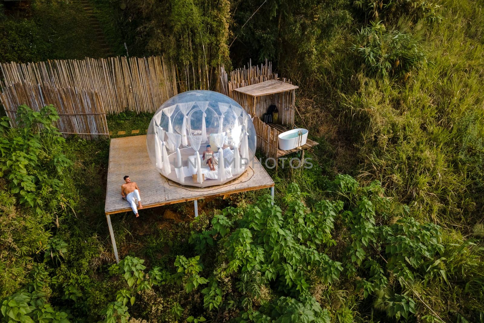 couple man and women in a bubble tent with an outdoor bathroom with a bath in the jungle rainforest. Luxury glamping in Thailand