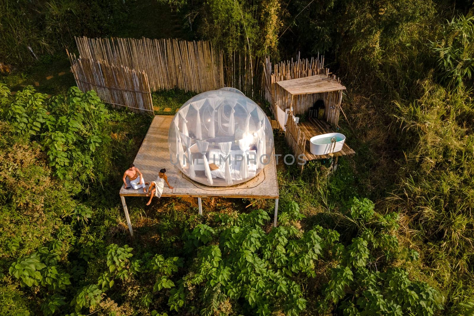 couple man and women in a bubble tent with an outdoor bathroom with bath in the jungle rainforest by fokkebok