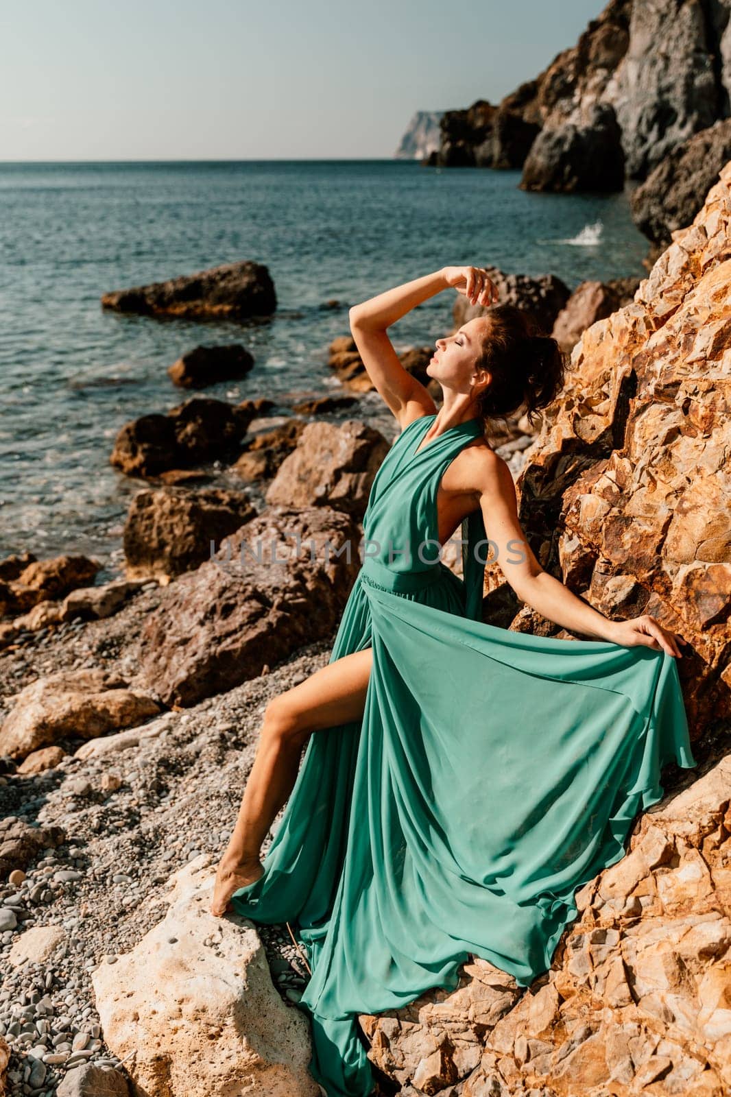 Woman green dress sea. Woman in a long mint dress posing on a beach with rocks on sunny day. Girl on the nature on blue sky background. by Matiunina