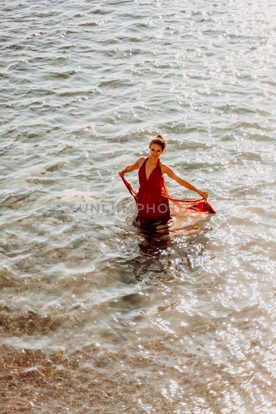 Woman red dress sea. Female dancer in a long red dress posing on a beach with rocks on sunny day.