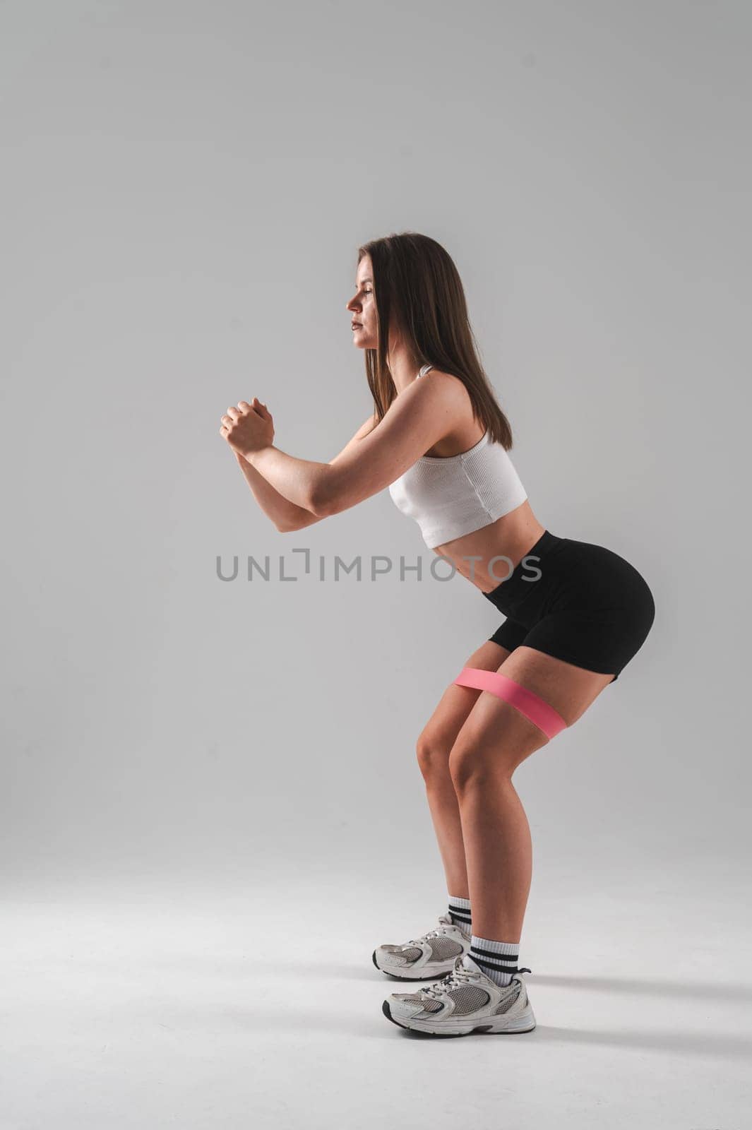 Caucasian woman doing squats with fitness band on white background. Vertical photo