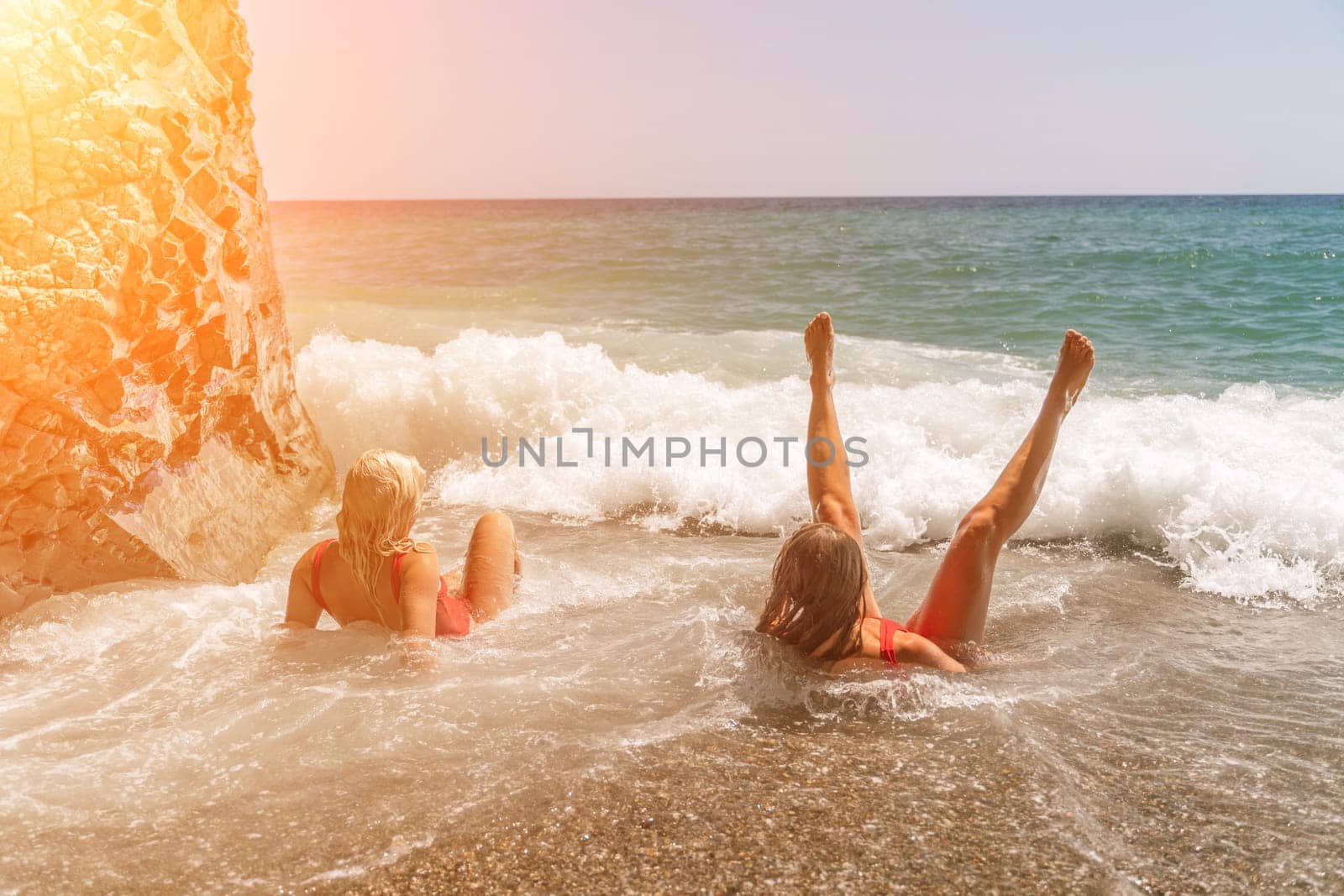 Women ocean play. Seaside, beach daytime, enjoying beach fun. Two women in red swimsuits enjoying themselves in the ocean waves. by Matiunina