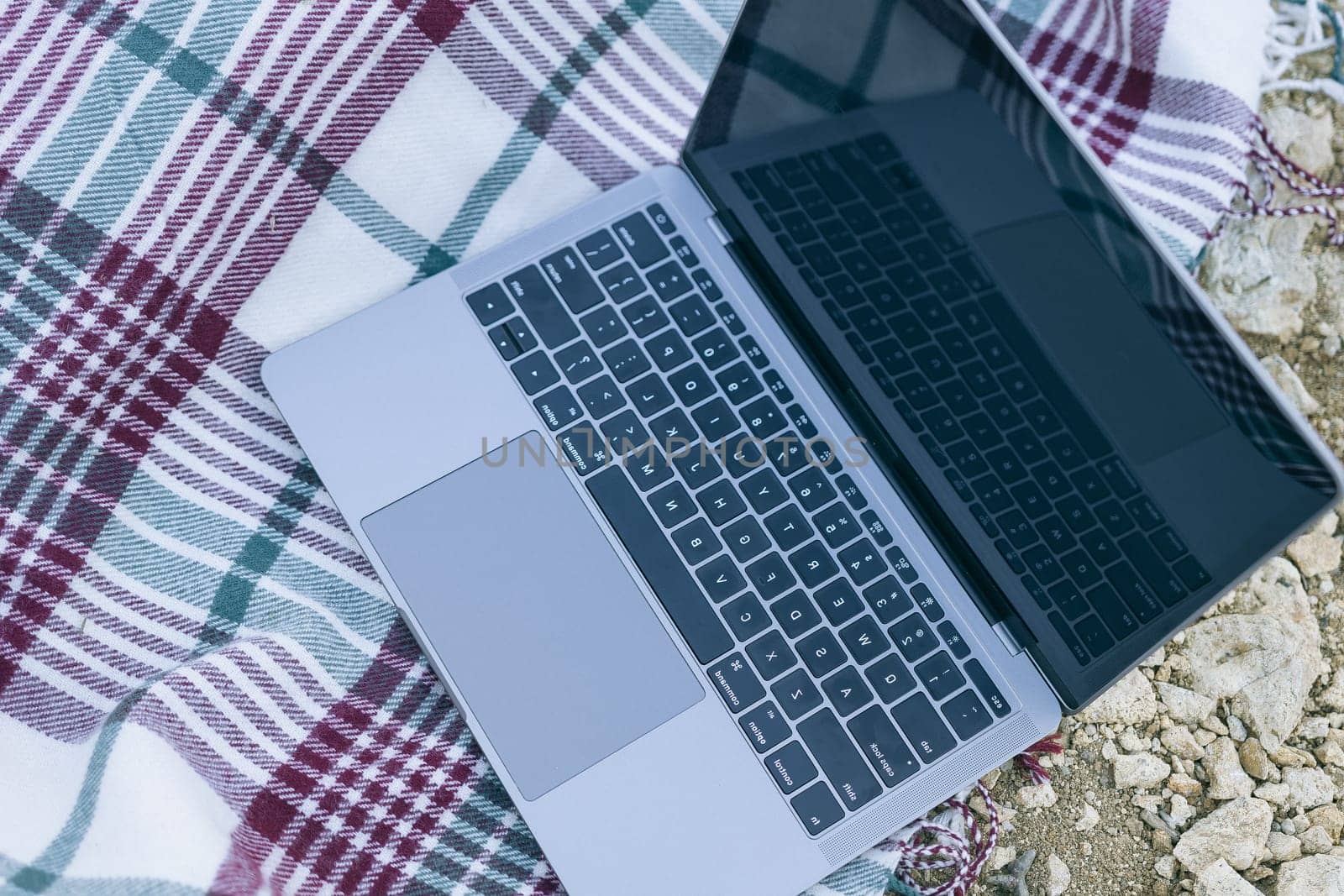 Laptop on blanket with ocean view. Illustrating serene outdoor laptop use. Freelancer enjoying their time outdoors while working or browsing the internet. by Matiunina