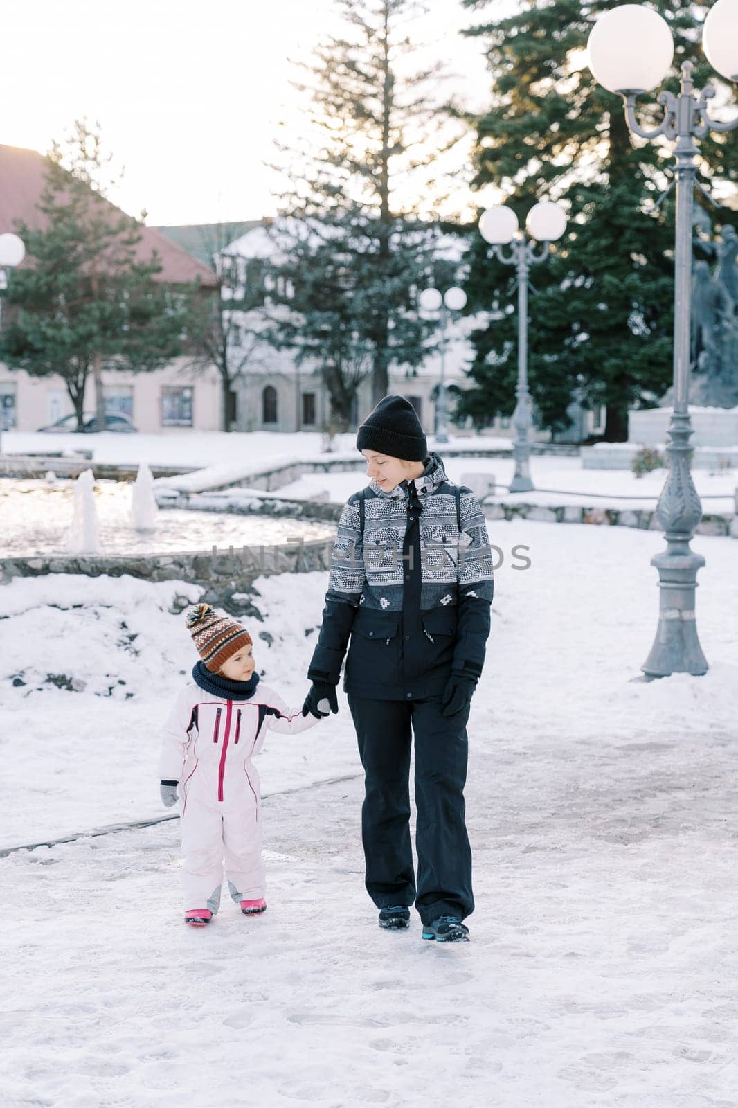 Mom and little girl walk holding hands along a snowy alley. High quality photo