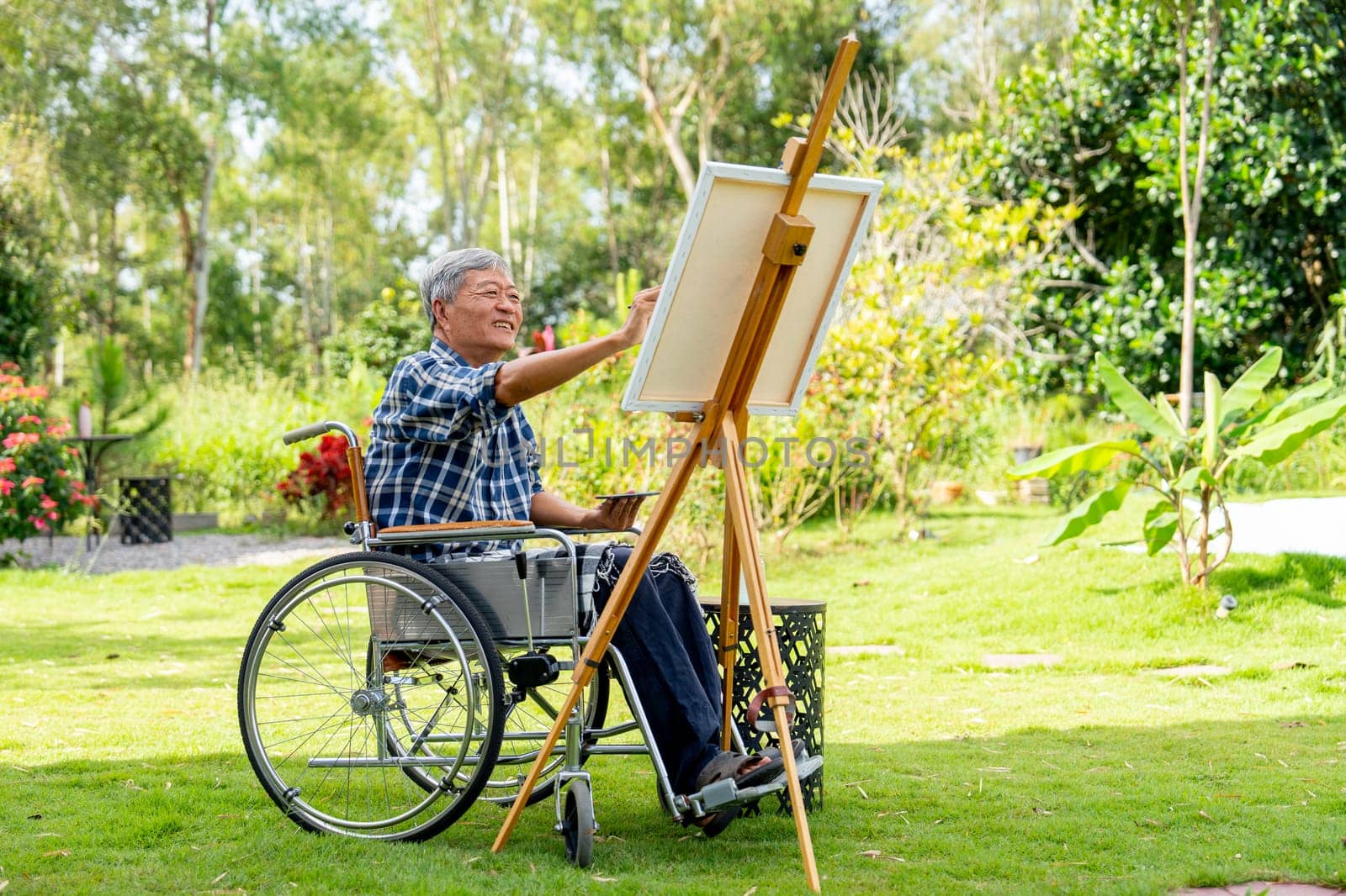 Asian senior man sit on wheelchair and paint the painting outdoor for relax and revive good health of old people outside.