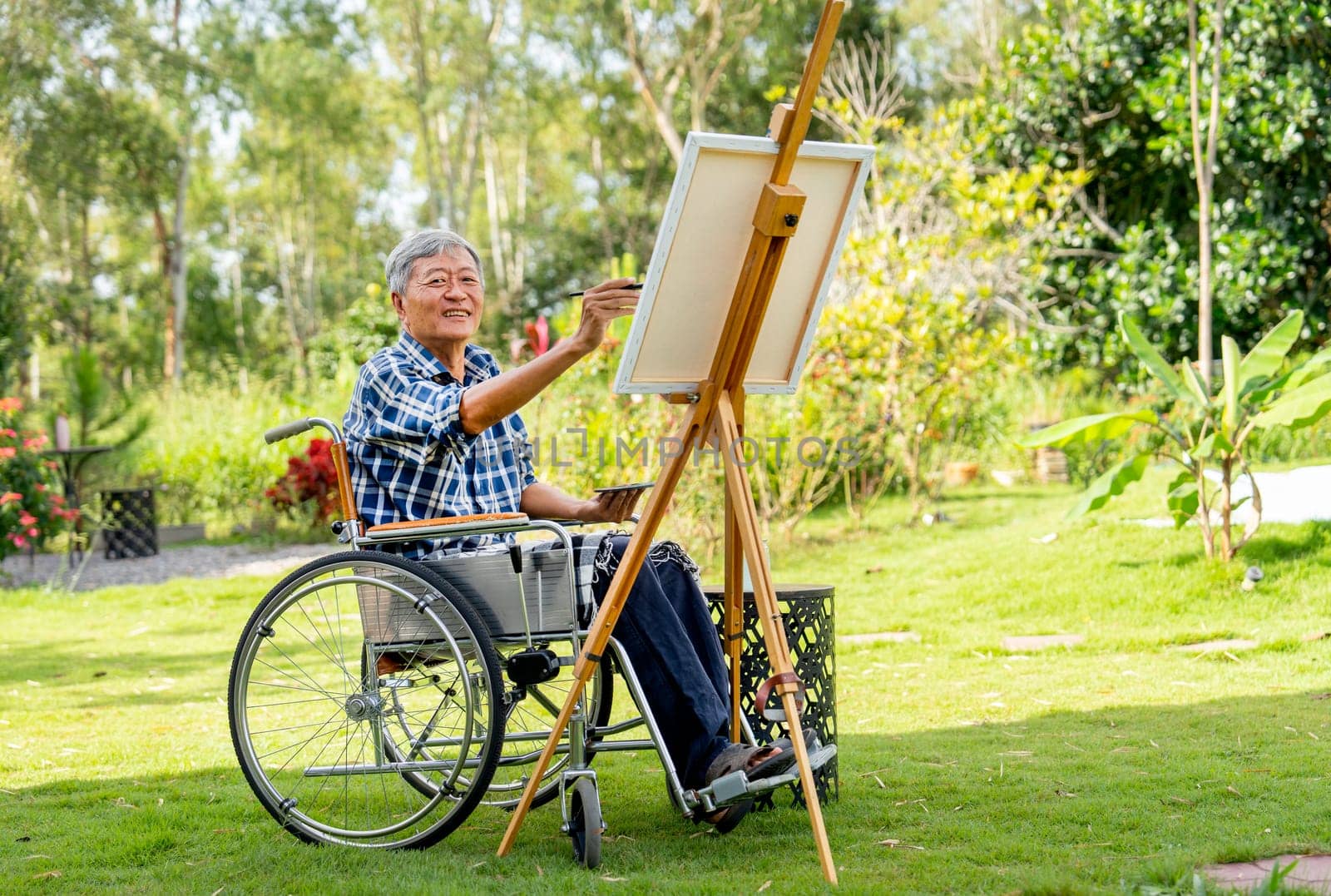 Front view of Asian senior man sit on wheelchair and paint the painting outdoor for relax and revive good health of old people outside.