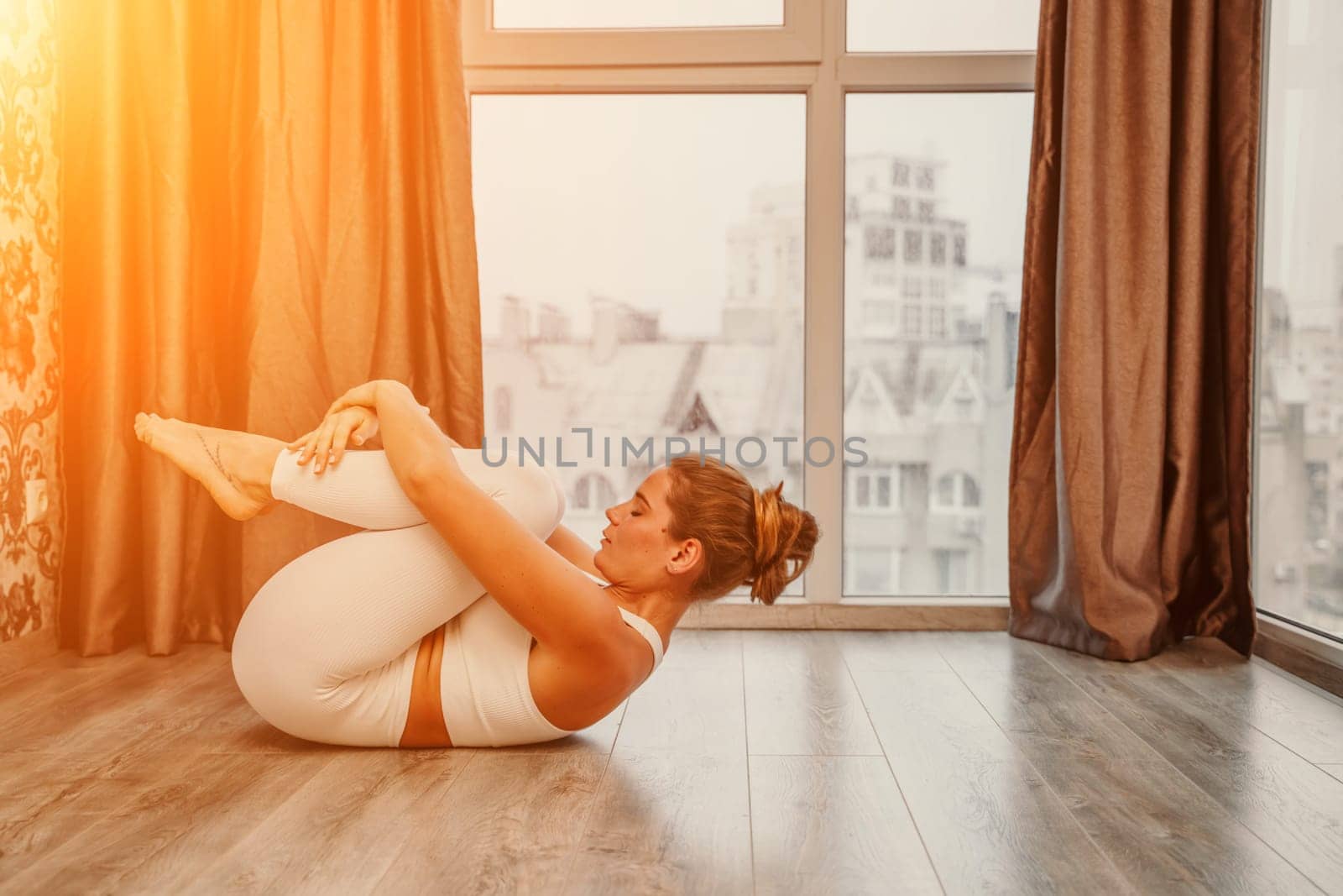 Young athletic attractive woman practicing yoga. Works out at home or in a yoga studio, sportswear, white pants and a full-length top indoors. Healthy lifestyle concept.