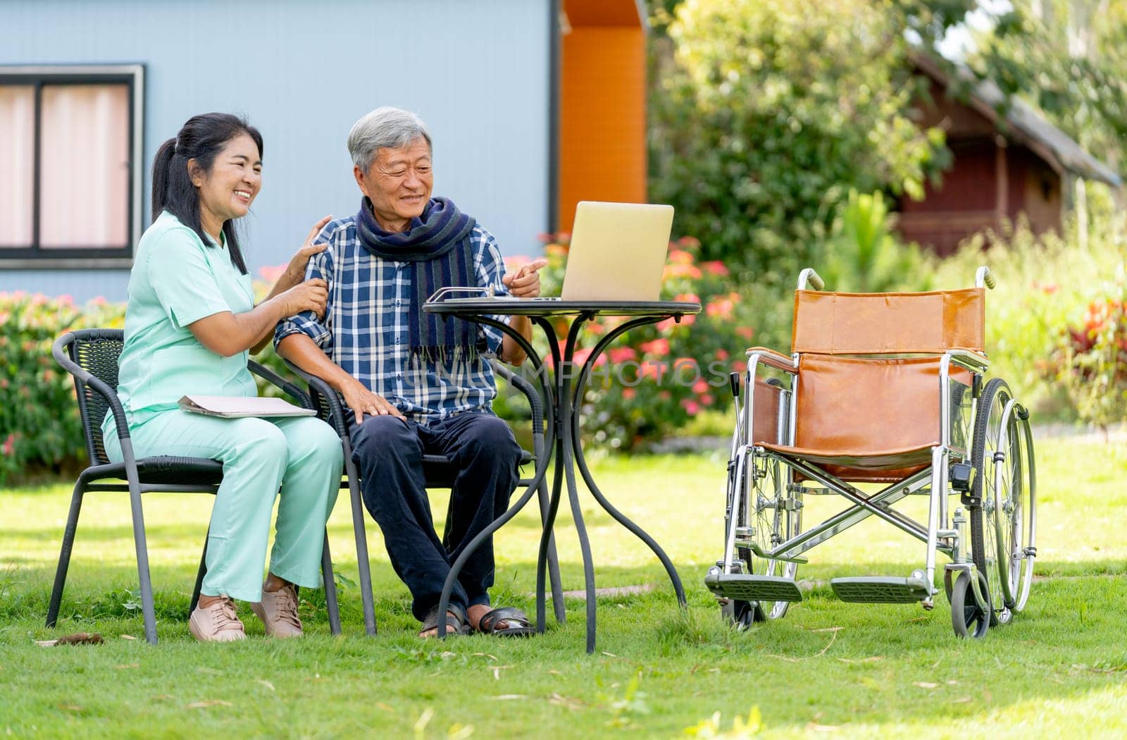 Asian senior man and nurse enjoy to watch the entertainment from laptop in area of garden with warm light.