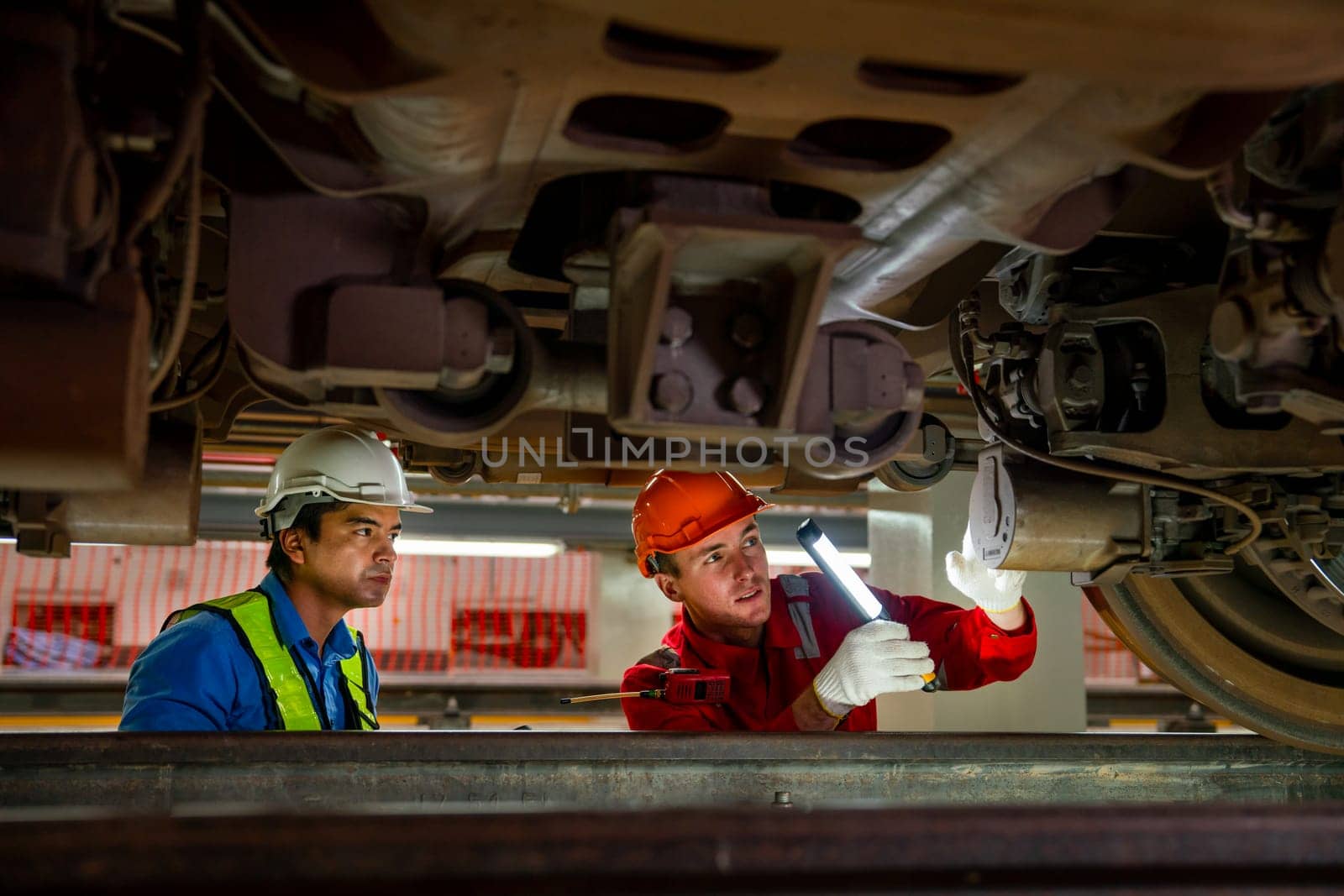 Professional engineer and technician workers check and maintenance under the train with use light tube to support in train factory workplace.