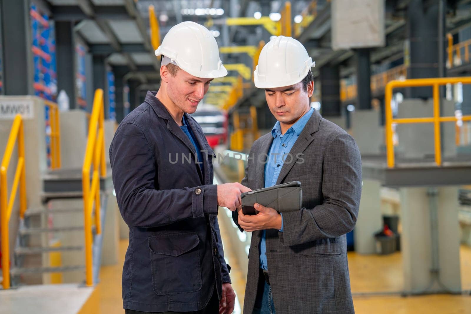 Professional manager or engineer workers discuss together with tablet in front of electrical or metro train in the factory.
