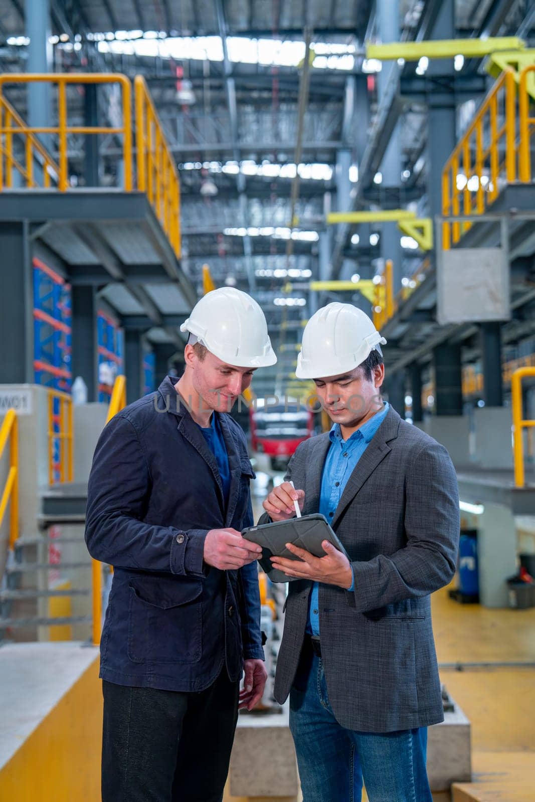 Vertical image of professional manager or engineer workers discuss together with tablet in front of electrical or metro train in the factory.