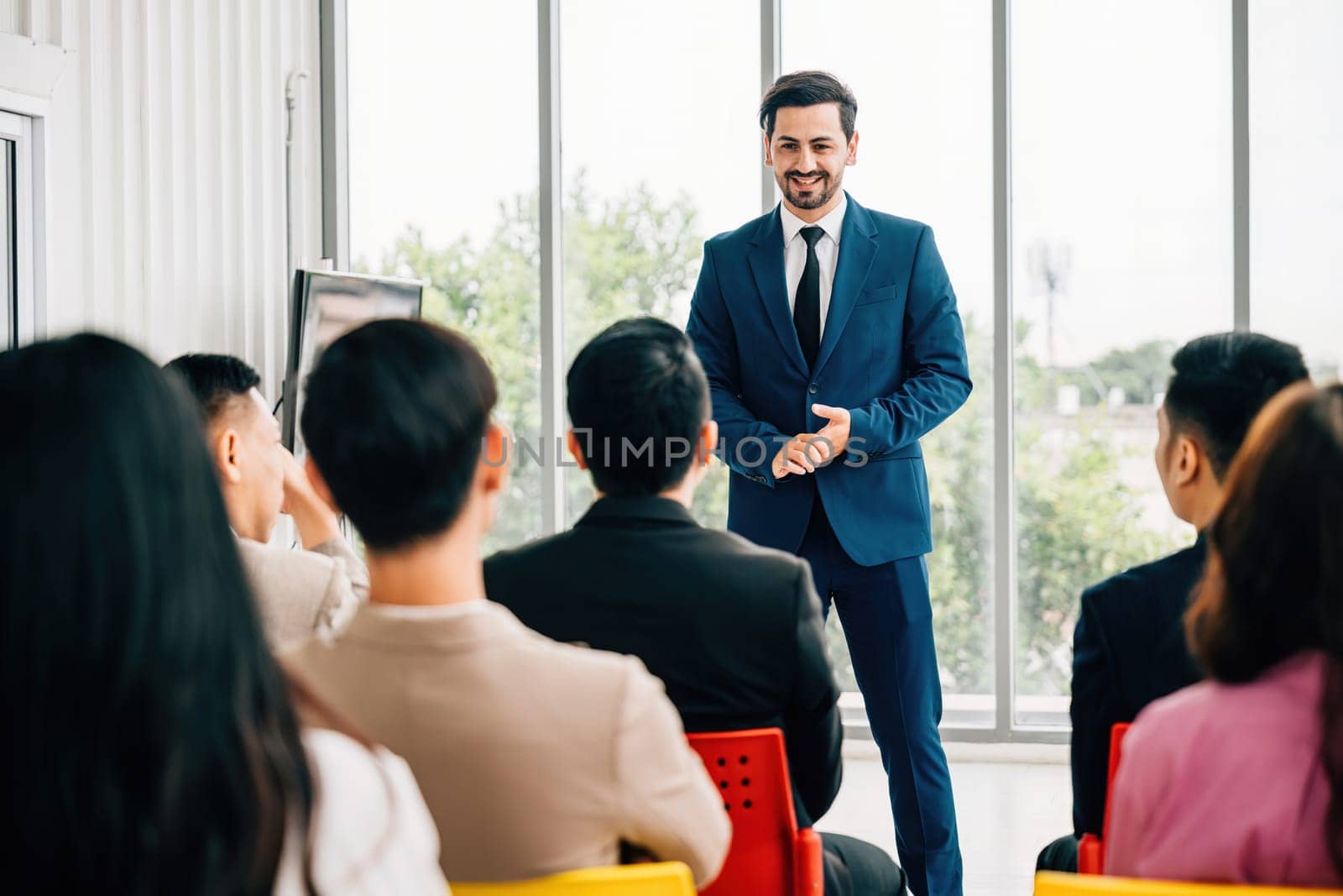 Business leaders present reviews in a meeting room, surrounded by a diverse group of colleagues actively listening. This embodies the concept of successful teamwork and collaboration.