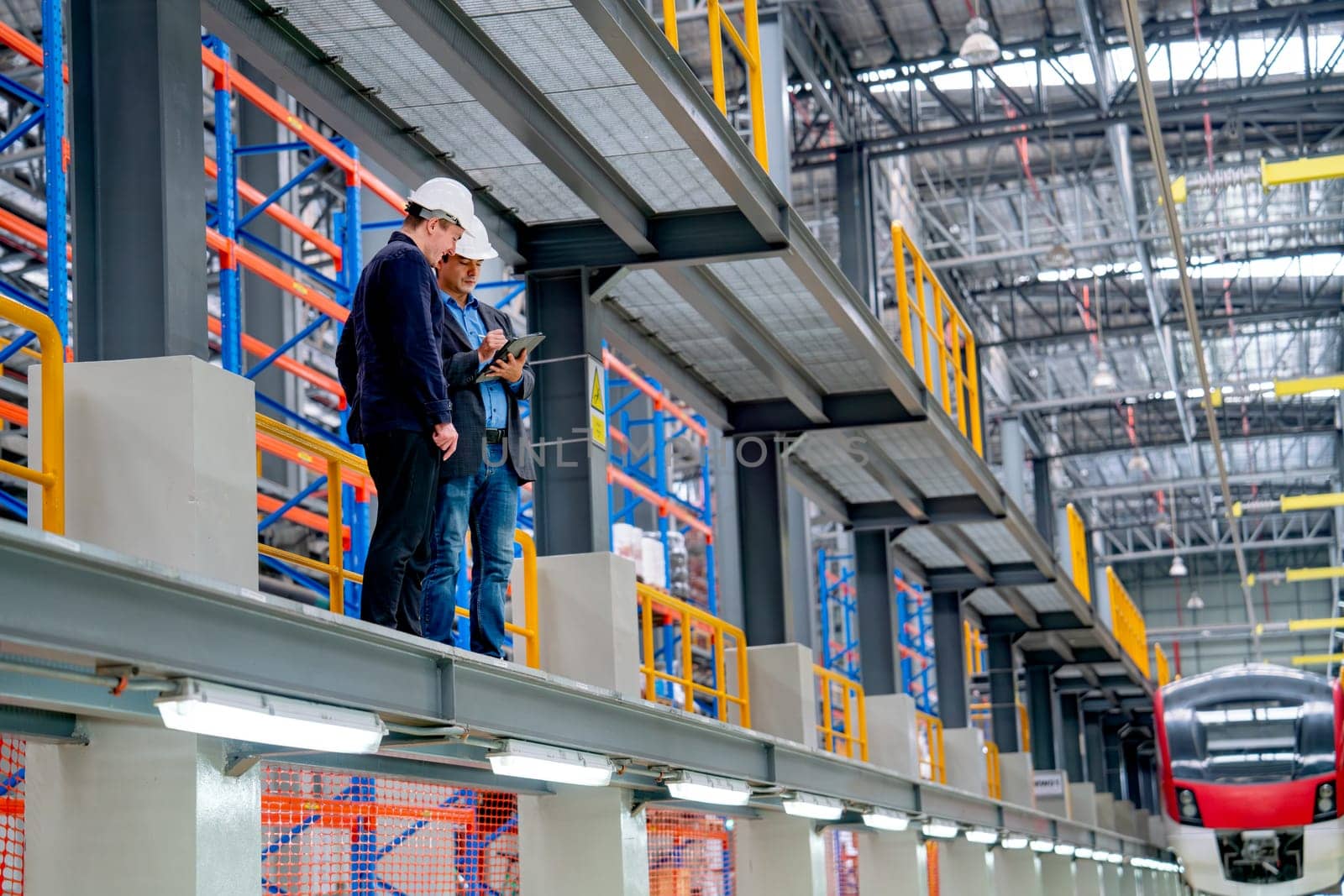 Professional technician and engineer workers stand near railroad tracks in front of electrical or metro train in factory workplace.