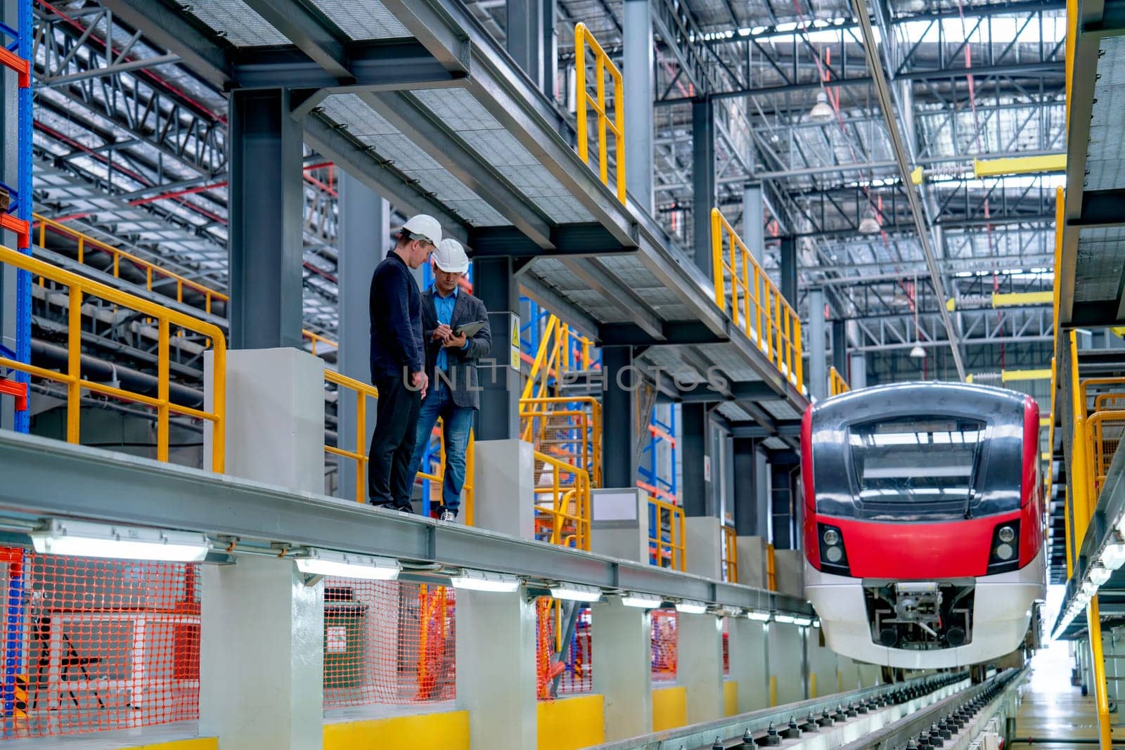 Wide shot of professional technician and engineer workers stand near railroad tracks in front of electrical or metro train in factory workplace.