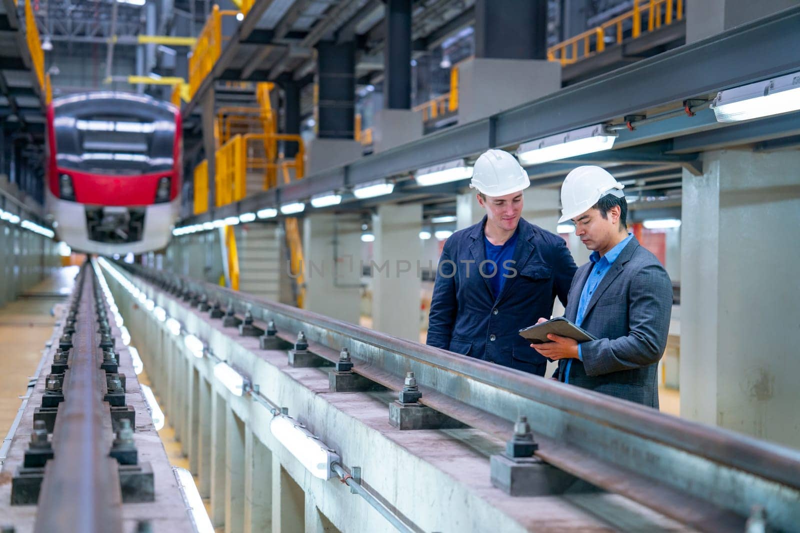 Professional manager or engineer workers discuss together with tablet near railroad tracks in front of electrical or metro train in the factory.