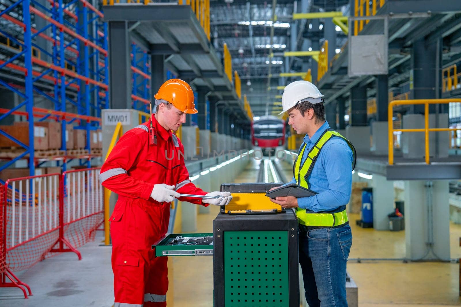 Professional technician and engineer worker discuss about tools and equipment with cabinet in front of railroad tracks of electrical or sky train in factory workplace.
