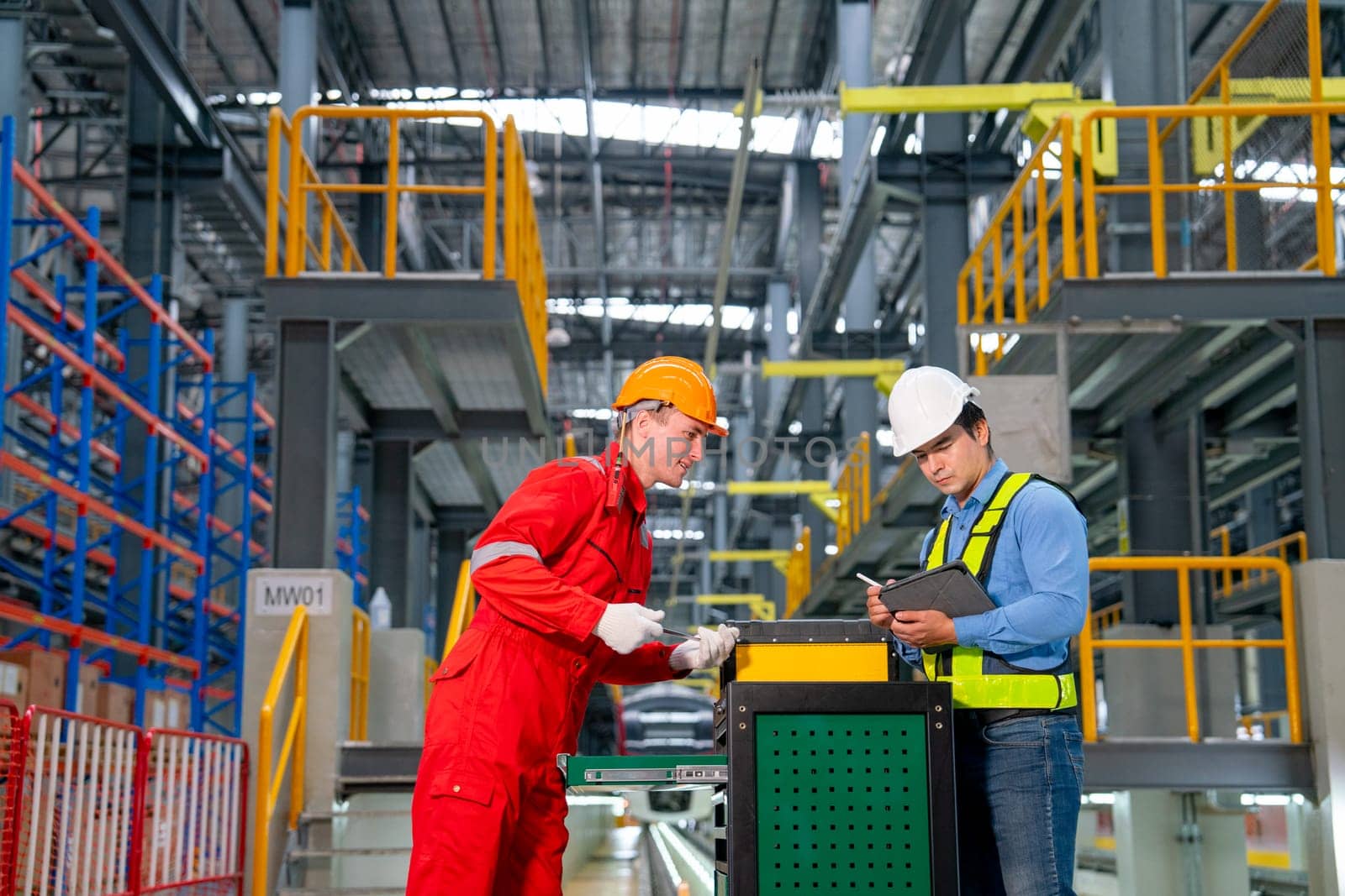 Professional technician and engineer worker discuss about tools and equipment with cabinet in front of railroad tracks of electrical or sky train in factory workplace.