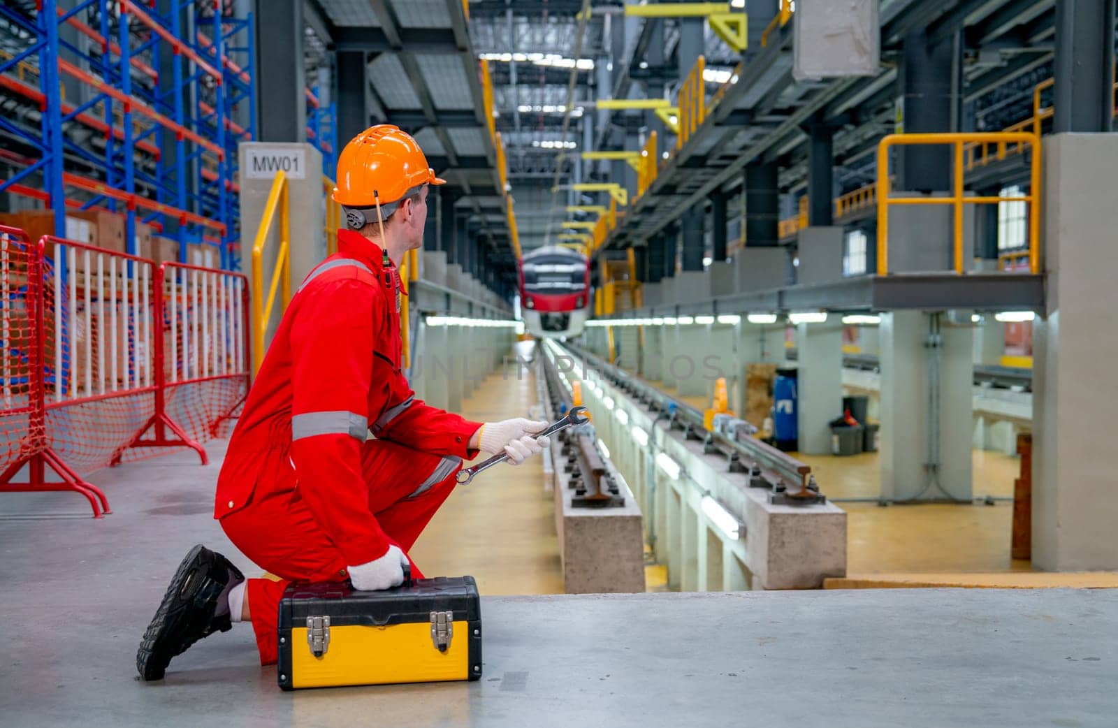 Wide shot and back of professional sit near railroad tracks of electrical or sky train also look to the train in the factory workplace.