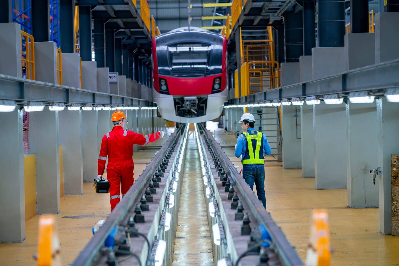 Back of professional engineer and technician stand near railroad tracks of electrical or sky train and discuss about accessories in their workplace.