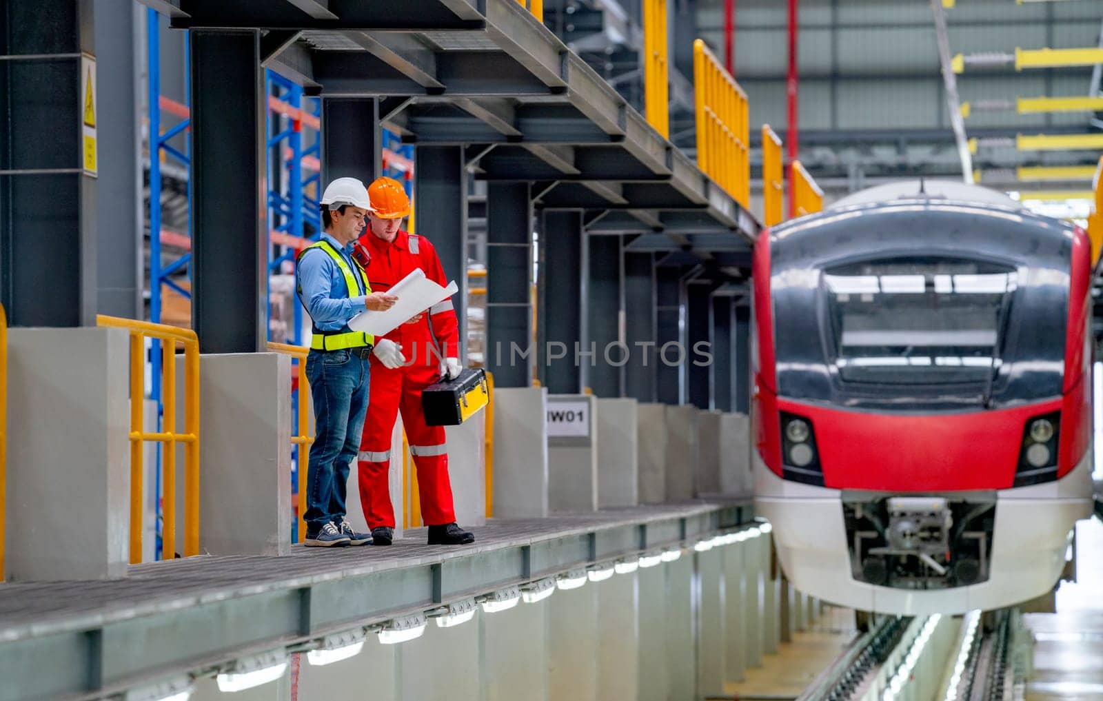 Professional engineer hold drawing plan and technician worker stay and discuss beside railroad tracks of electrical or sky train in factory workplace.