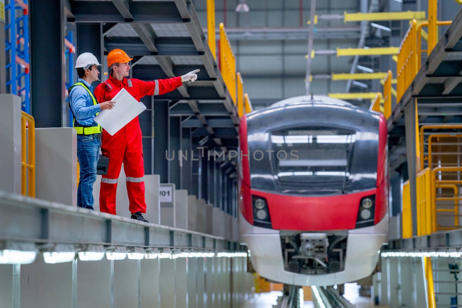Professional technician point to right direction and discuss with engineer near railroad tracks of electrical or sky train in factory workplace.