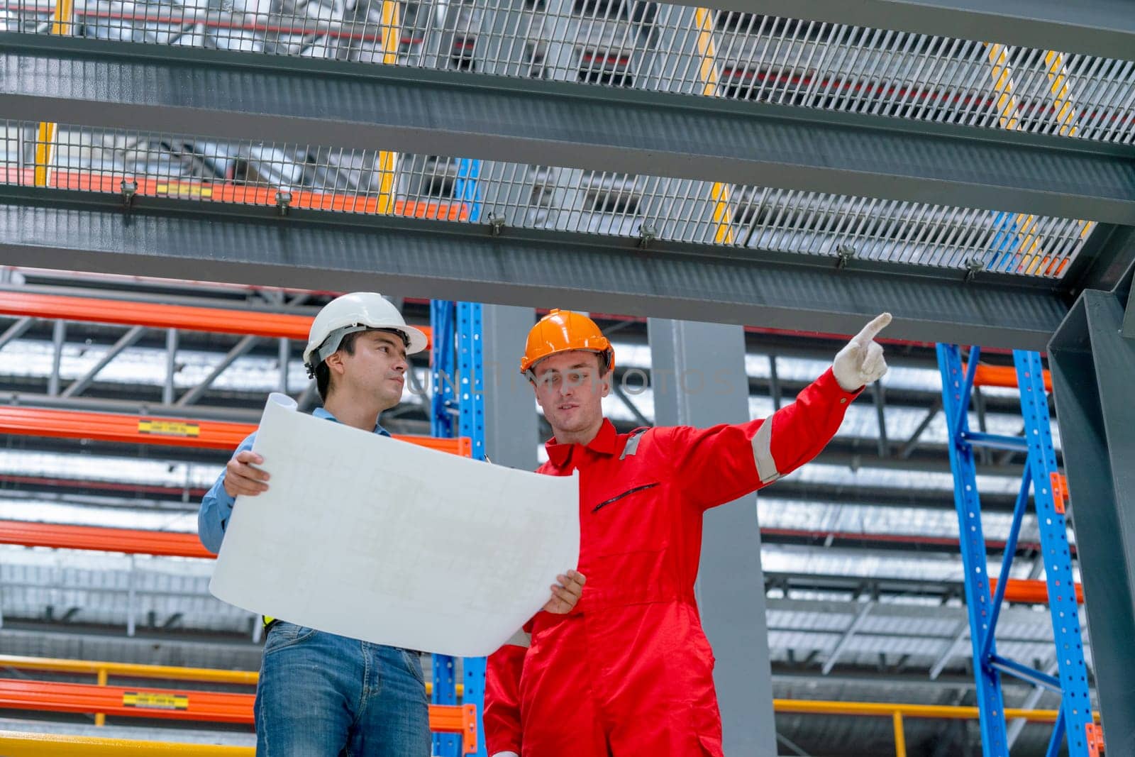 Close up and lower view engineer hold drawing plan and technician worker stay near railroad tracks of electrical or sky train in factory workplace.