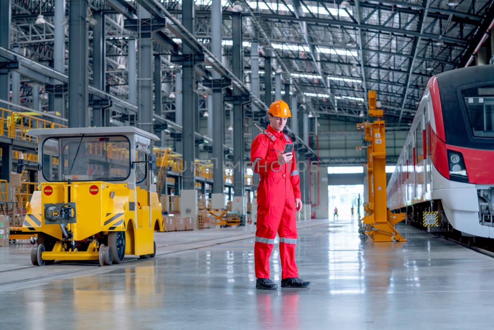 Professional technician worker stand near factory truck and hold and look to mobile phone in electrical or metro train factory. Concept of communication during work in industrial workplace.