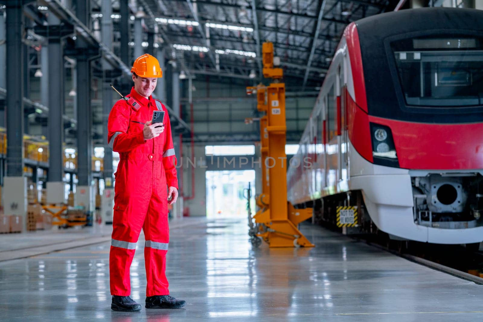 Professional technician worker stand near the train and hold and look to mobile phone in electrical or metro train factory.