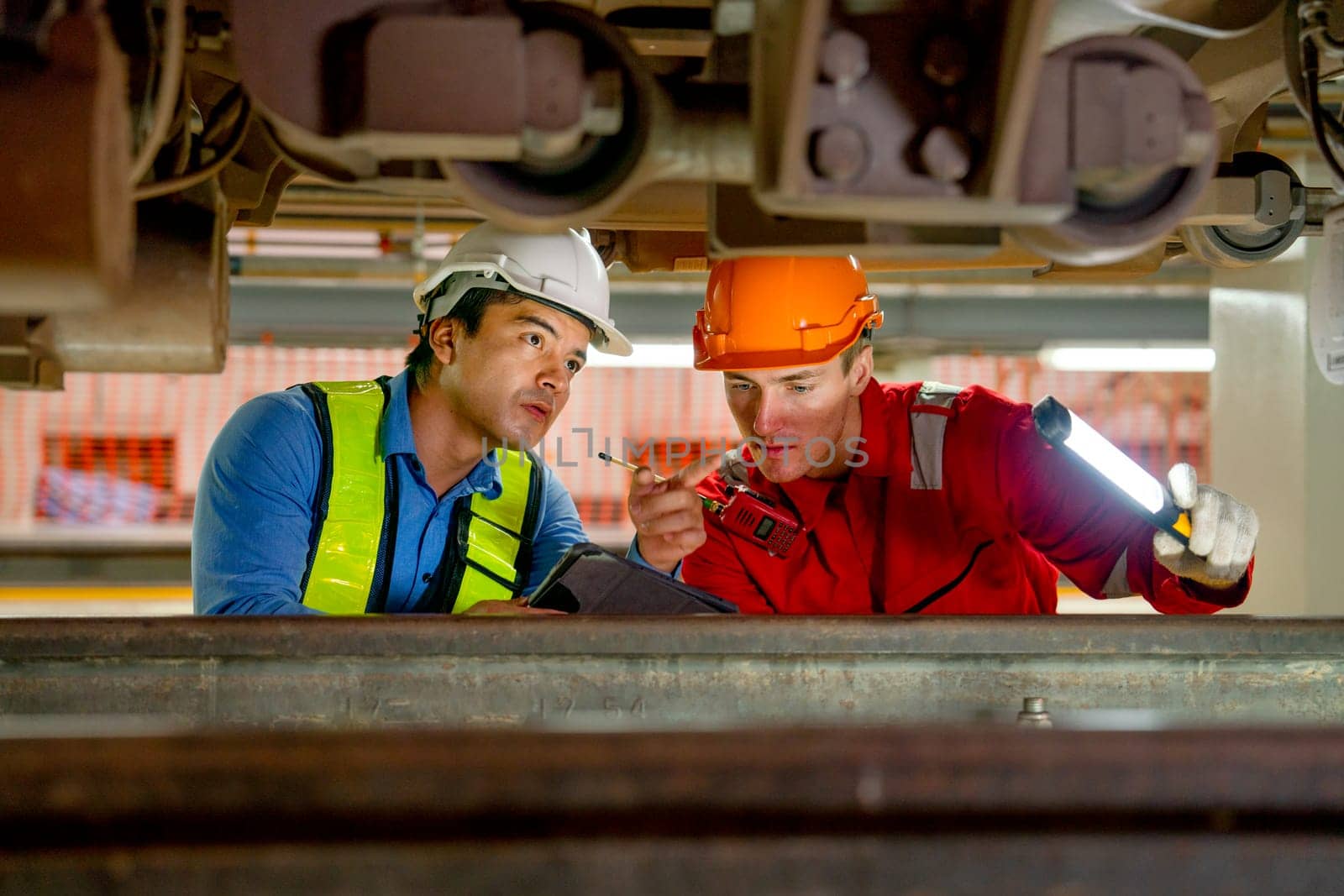 Professional engineer and technician workers check and maintenance under the train with use light tube and tablet to support in train factory workplace.