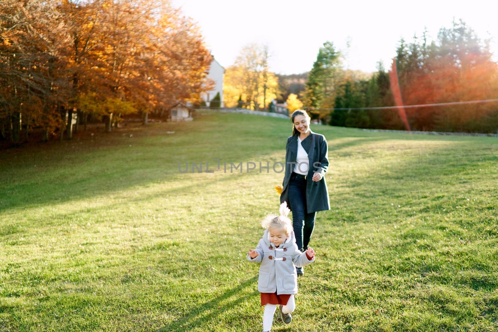 Smiling mother follows a little running girl through a green meadow. High quality photo