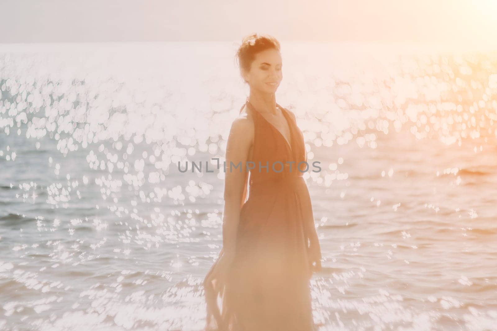 Woman in red dress on sea. Side view a Young beautiful sensual woman in a red long dress posing on the beach near sea on sunset. Girl on the nature on blue sky background. Fashion photo. by panophotograph