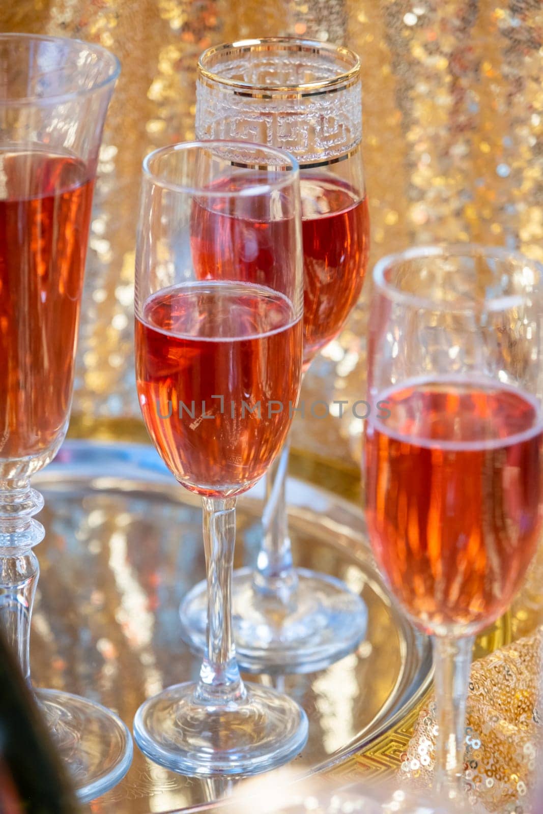 alcohol drinks concept. glasses of rose champagne and bottle on the tray on sparkling golden tablecloth