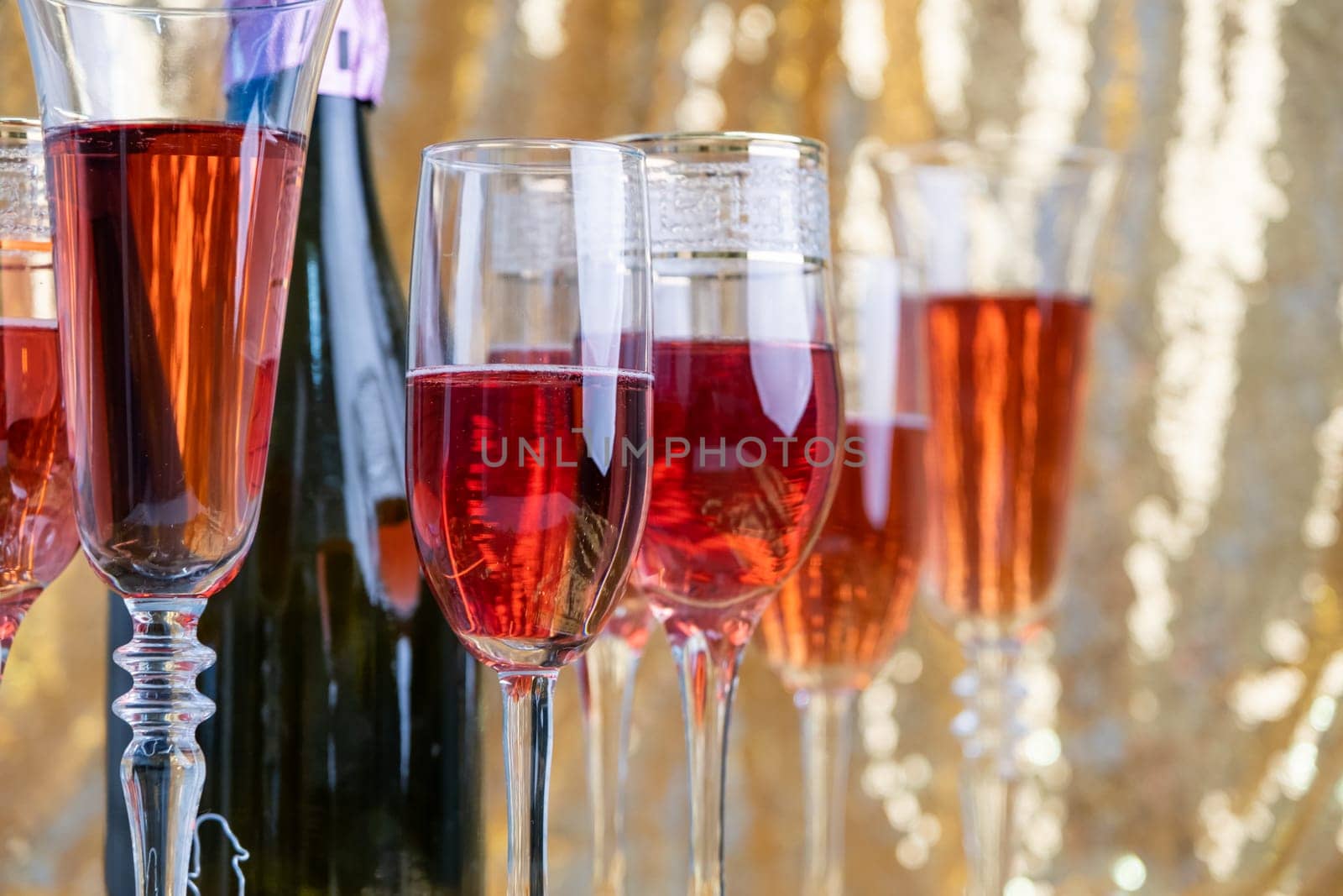 alcohol drinks concept. glasses of rose champagne and bottle on the tray on sparkling golden tablecloth