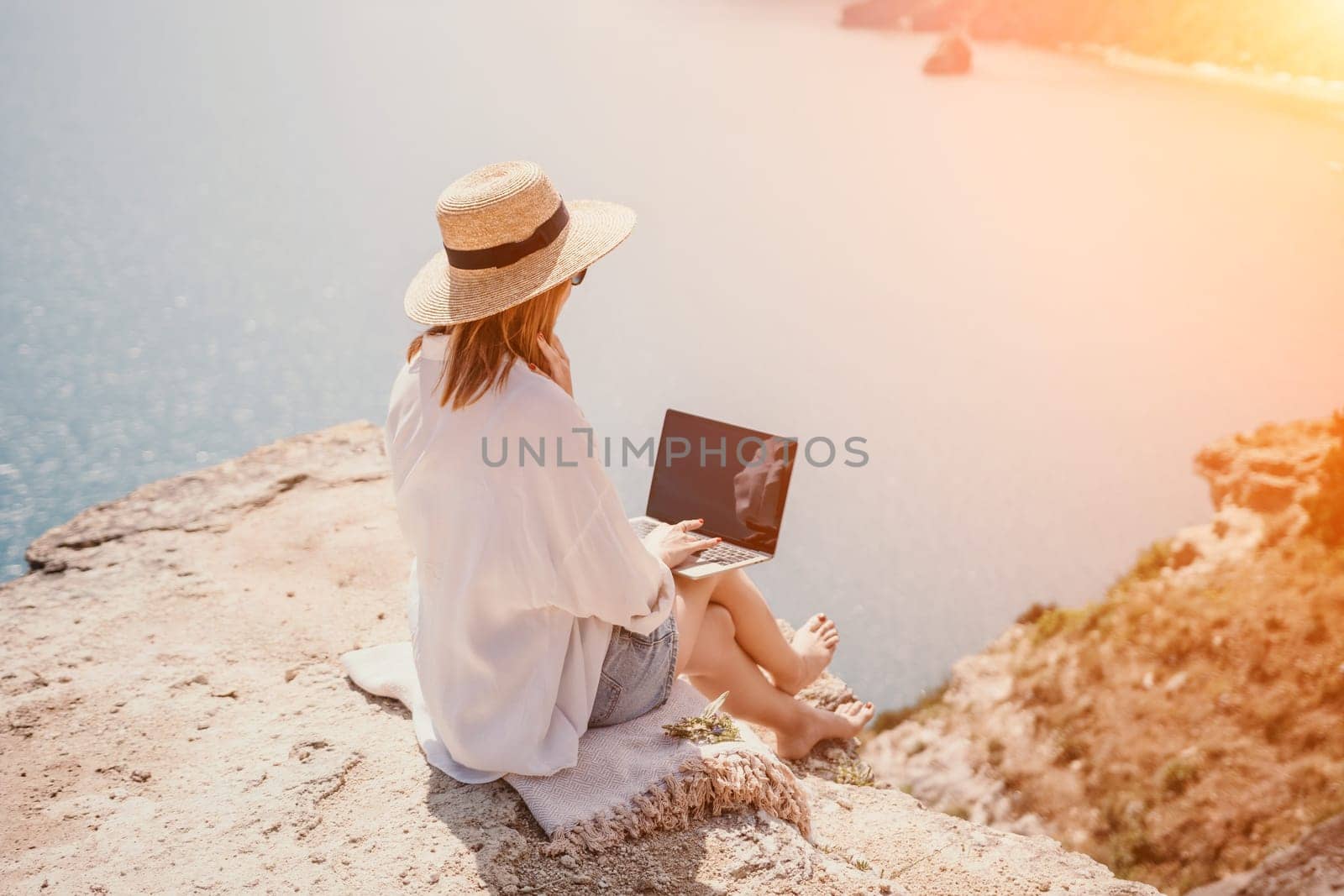 Woman sea laptop. Successful business woman working on laptop by the sea. Pretty lady typing on computer at summer day outdoors. Freelance, digital nomad, travel and holidays concept. by panophotograph