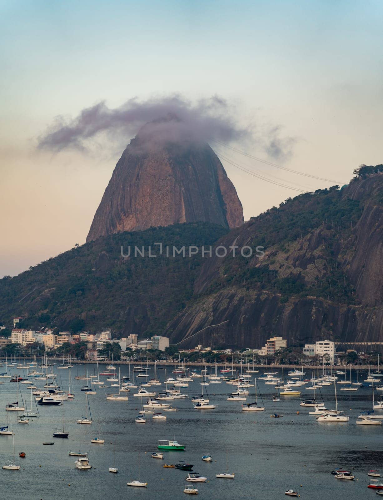 Cloud-shrouded Sugarloaf Mountain overlooks serene bay with boats at dusk in Rio.